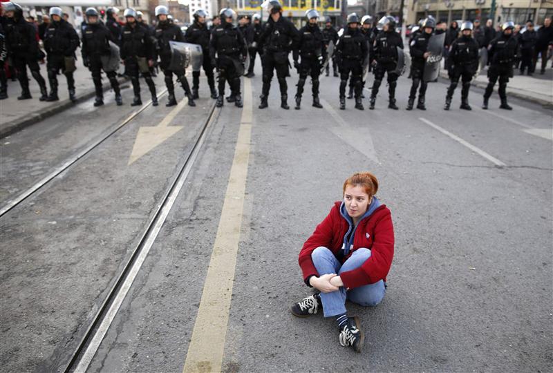 An anti-government protester sits on the ground in front of police during a demonstration in Sarajevo